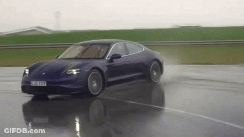 A Blue Porsche Taycan Is Driving Down A Wet Road . GIF