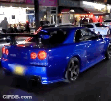 A Blue Sports Car Is Parked On The Street In Front Of A Store Called Rio GIF