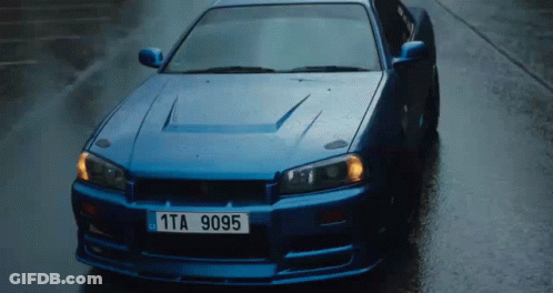A Blue Sports Car With A License Plate That Says 1Ta 9095 Is Driving Down A Wet Street . GIF