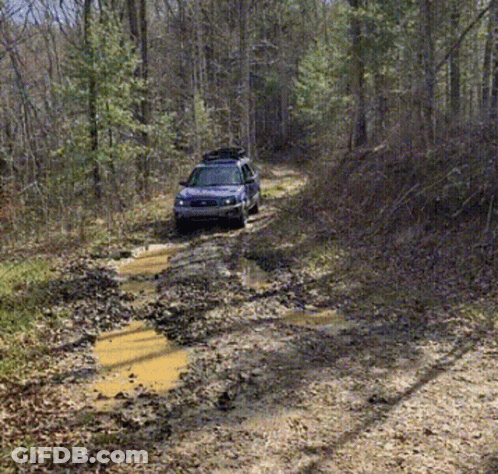A Blue Suv With A Roof Rack Is Driving Down A Muddy Road GIF