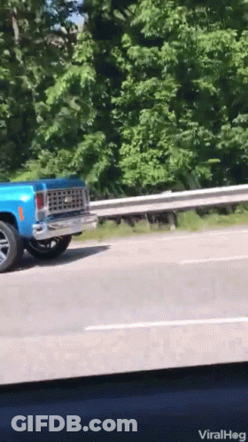 A Blue Truck Is Driving Down A Highway With A Railing Behind It GIF