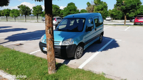 A Blue Van Is Parked In A Parking Lot With A Tree In The Foreground GIF