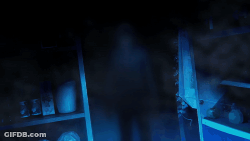 A Blurred Image Of A Person Standing In A Dark Room With A Blue Light Behind Them GIF
