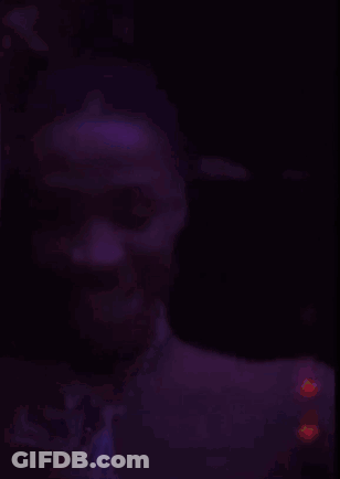 A Blurry Picture Of A Man In A Dark Room With Purple Lights Behind Him GIF