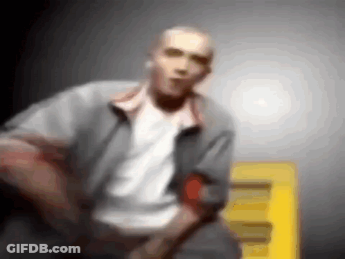 A Blurry Picture Of A Man In A Gray Jacket And White Shirt Standing Next To A Yellow Sign . GIF