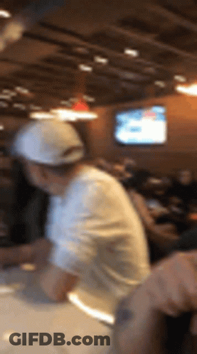 A Blurry Picture Of A Man In A White Hat Making Pizza GIF