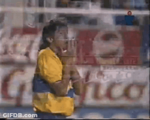 A Blurry Picture Of A Man In A Yellow Shirt Standing In Front Of A Sign That Says ' Coca Cola ' GIF