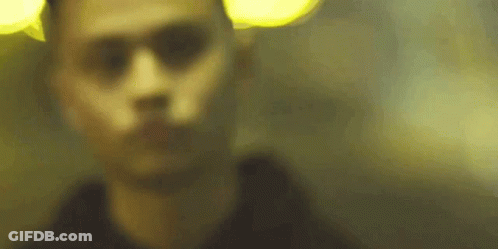 A Blurry Picture Of A Man 'S Face In A Dark Room With A Yellow Light Behind Him . GIF