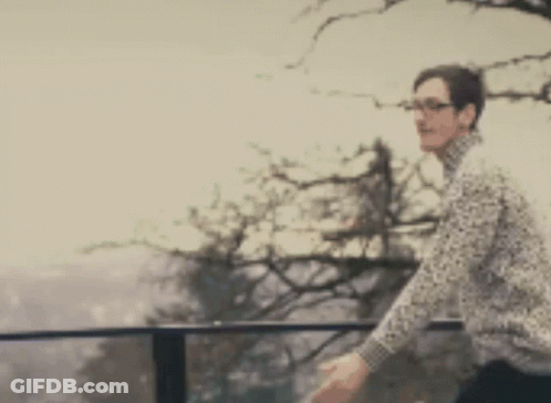 A Blurry Picture Of A Man Standing On A Balcony With A Tree In The Background GIF
