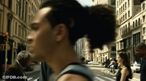 A Blurry Picture Of A Man Walking Down A Street With A Woman Riding A Bike GIF