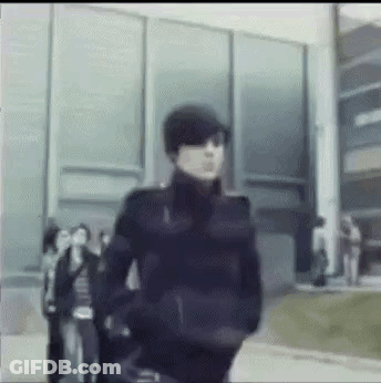 A Blurry Picture Of A Man Wearing Sunglasses And A Hat Walking In Front Of A Building . GIF