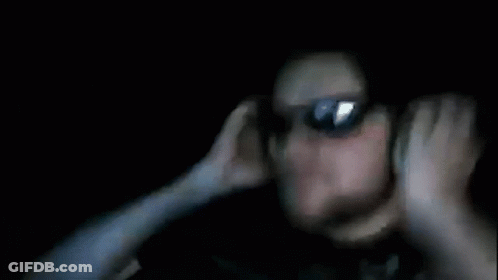 A Blurry Picture Of A Person Covering Their Ears In The Dark GIF