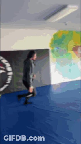 A Blurry Picture Of A Person Running On A Blue Mat In A Gym GIF