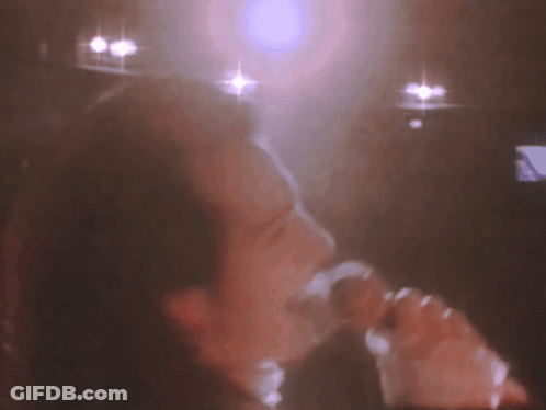 A Blurry Picture Of A Person Singing Into A Microphone . GIF