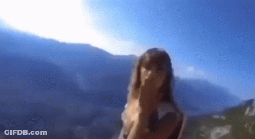 A Blurry Picture Of A Woman Covering Her Face In Front Of A Mountain Range . GIF