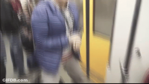 A Blurry Picture Of A Woman In A Blue Jacket Walking On A Train GIF