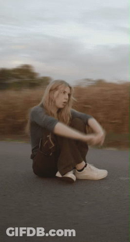 A Blurry Picture Of A Woman Sitting On The Side Of A Road GIF