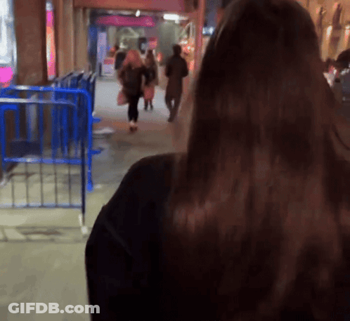 A Blurry Picture Of A Woman Walking Down A Street At Night GIF