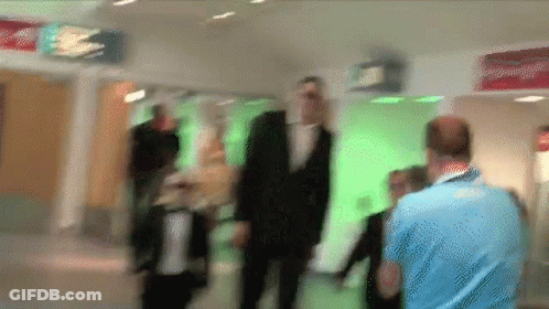 A Blurry Picture Of People Walking In A Hallway With A Red Sign That Says Exit GIF