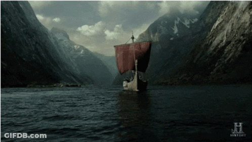 A Boat With A Red Sail Is Floating In A River With Mountains In The Background GIF