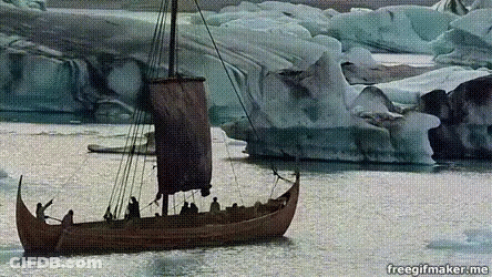 A Boat With A Sail Is In The Water With Icebergs In The Background GIF