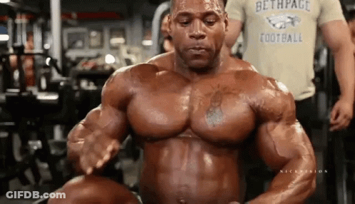 A Bodybuilder Is Flexing His Muscles In A Gym While Wearing A Football Shirt . GIF