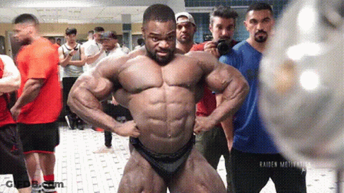 A Bodybuilder Is Posing For A Picture In Front Of A Group Of People . GIF