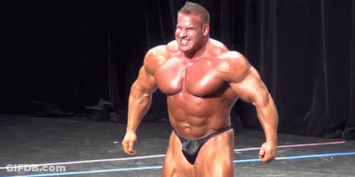 A Bodybuilder Is Standing On A Stage With His Arms In The Air GIF