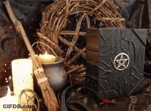 A Book With A Pentagram On It Sits On A Table Next To Candles And A Broom GIF