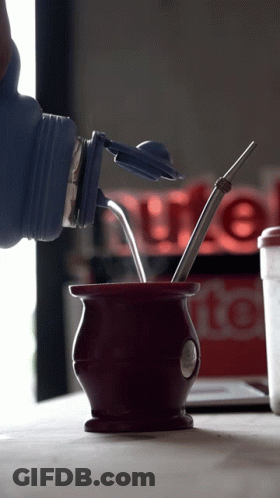 A Bottle Is Being Poured Into A Cup With A Straw In It GIF