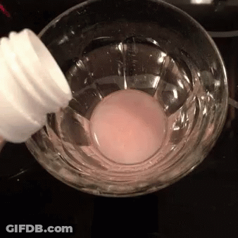 A Bottle Is Being Poured Into A Glass Of Liquid GIF