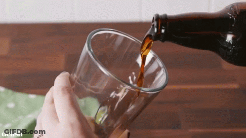 A Bottle Of Beer Is Being Poured Into A Glass By A Person GIF