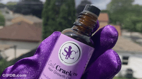 A Bottle Of Coil Crack Hair Growth Oil Is Being Held In A Purple Glove GIF