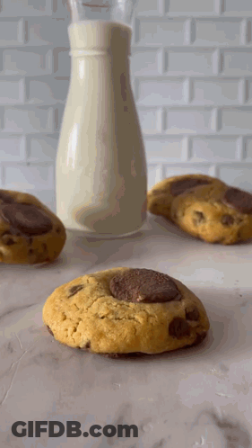 A Bottle Of Milk Sits Next To Three Cookies GIF