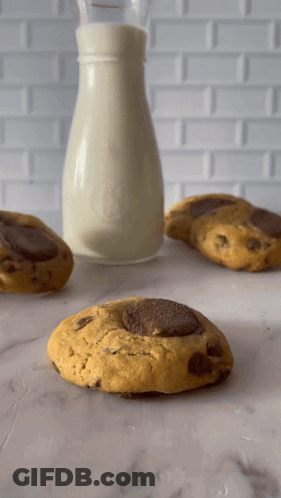 A Bottle Of Milk Sits Next To Three Cookies GIF