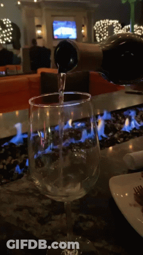 A Bottle Of Wine Is Being Poured Into A Glass On A Table GIF