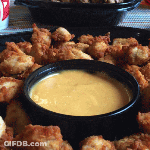 A Bowl Of Cheese Sauce Sits Next To A Tray Of Chicken Nuggets GIF