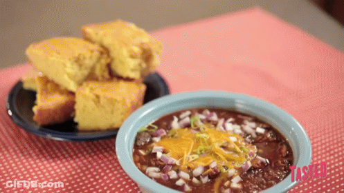 A Bowl Of Chili Sits On A Table Next To A Bowl Of Cornbread GIF