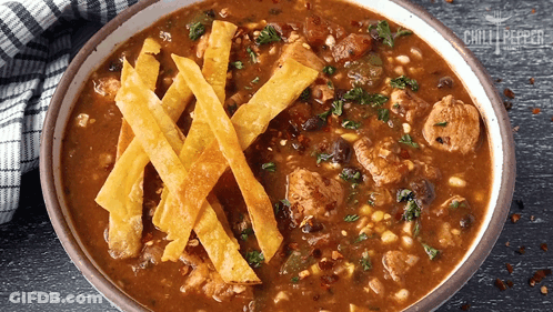 A Bowl Of Chili With Tortilla Strips On Top Of It GIF