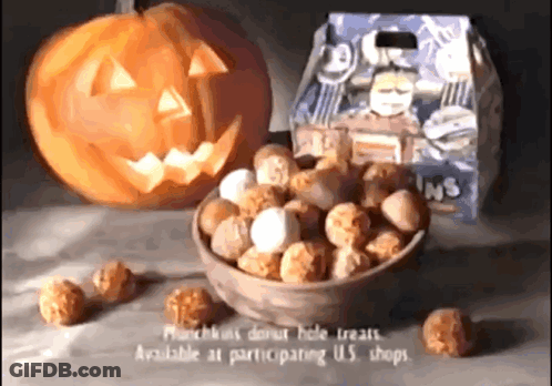 A Bowl Of Donut Hole Treats Next To A Pumpkin With A Face Carved Into It GIF