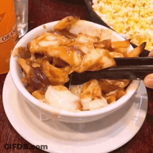 A Bowl Of Food With Tongs On A Plate With A Bottle Of Orange Juice In The Background GIF