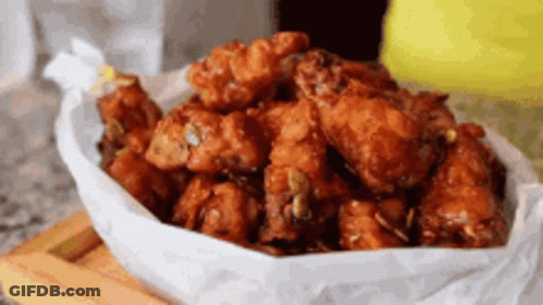A Bowl Of Fried Chicken Wings Wrapped In Wax Paper On A Wooden Cutting Board . GIF