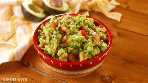 A Bowl Of Guacamole Sits On A Wooden Table Next To A Pile Of Tortilla Chips GIF