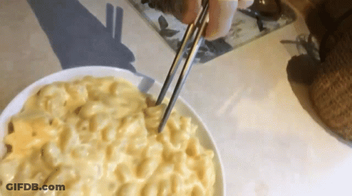 A Bowl Of Macaroni And Cheese Is Being Served With Chopsticks GIF