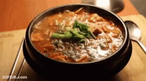 A Bowl Of Soup Is Sitting On A Wooden Table Next To Chopsticks And A Spoon . GIF