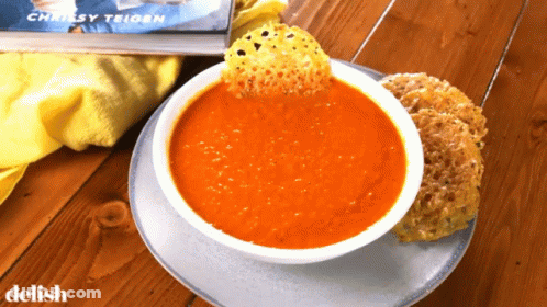 A Bowl Of Tomato Soup Next To A Book By Chrissy Trigon GIF
