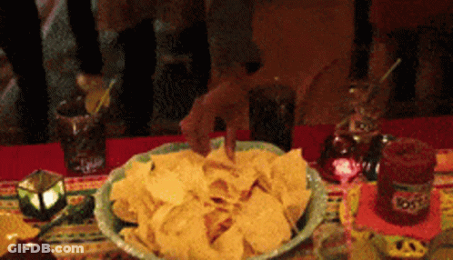 A Bowl Of Tortilla Chips Sits On A Table Next To A Bottle Of Tequila GIF