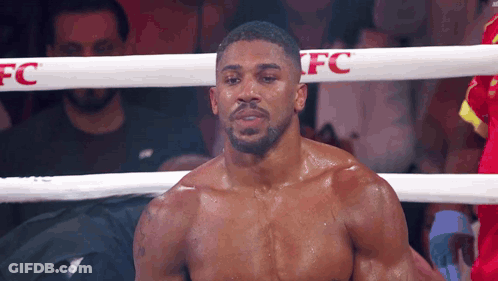 A Boxer Without A Shirt Is Standing In A Boxing Ring Looking At The Camera . GIF