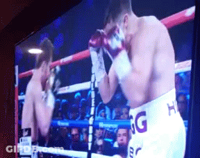 A Boxing Match Is Being Shown On A Television And One Of The Fighters Is Wearing Shorts That Say Hg GIF