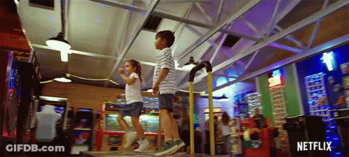 A Boy And A Girl Are Jumping On A Dance Floor In An Amusement Park . GIF